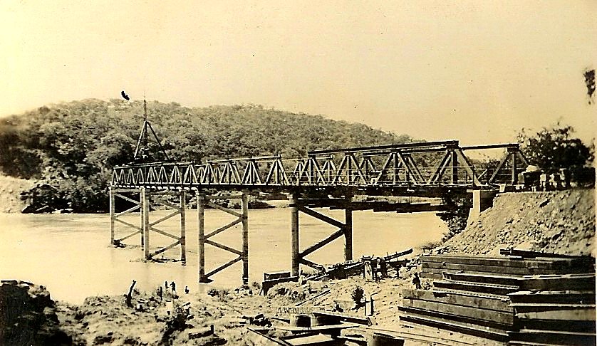 A steel truss road bridge under construction across a river